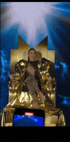 a woman is sitting on a golden throne with a m on her head