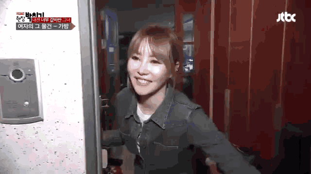 a woman is smiling while standing in front of a door that says jtbc on it .