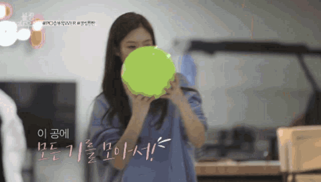 a woman is blowing up a green balloon with korean writing on the bottom