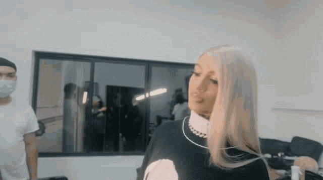 a woman with long blonde hair is standing in a room with a man in a mask .