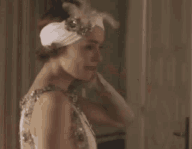 a woman in a white dress and feather headband is standing in front of a mirror .