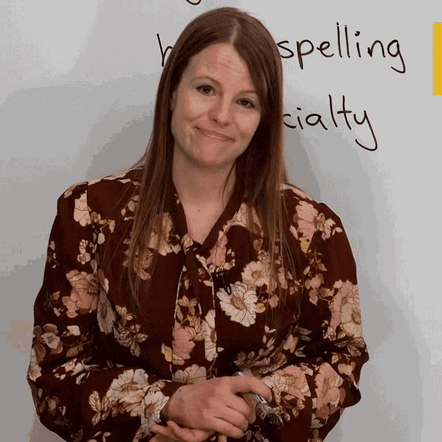 a woman in a floral shirt stands in front of a white board with spelling specialty written on it