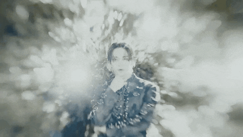 a black and white photo of a man in a black jacket standing in front of a blurred background .