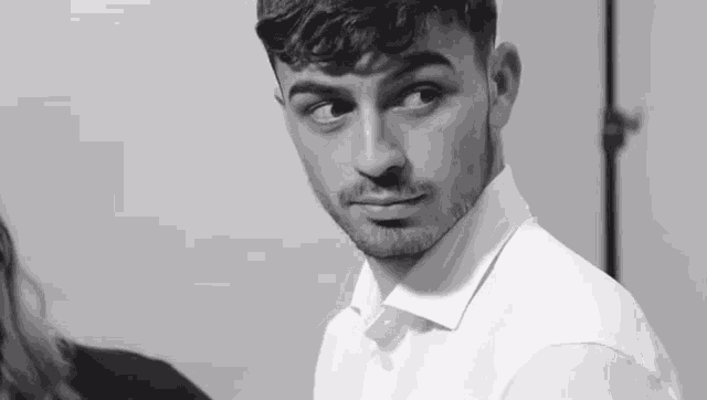 a black and white photo of a young man in a white shirt looking at the camera .
