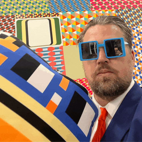 a man in a suit and tie is wearing sunglasses and holding a colorful pillow