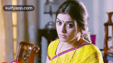 a woman in a yellow saree is making a funny face while sitting at a table .
