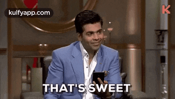 a man in a blue suit is sitting in a chair holding a cell phone and smiling .