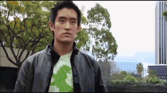a man wearing a green shirt with a dragon on it is standing in front of trees