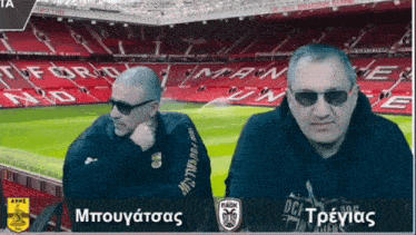 two men wearing sunglasses are sitting in front of a soccer field with the words " μπουργατσασ " on the bottom