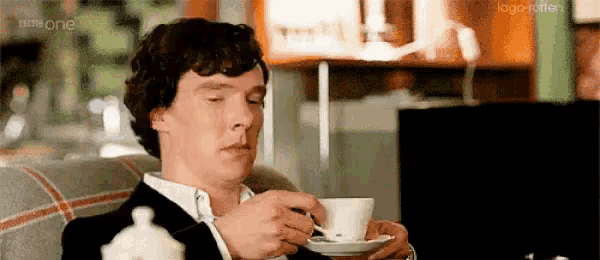a man is sitting on a couch drinking a cup of tea with a spoon .