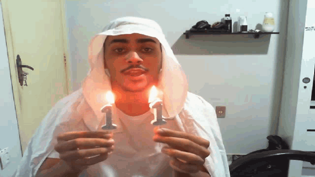a man wearing a white cape is holding two lit candles with the number 1 on them