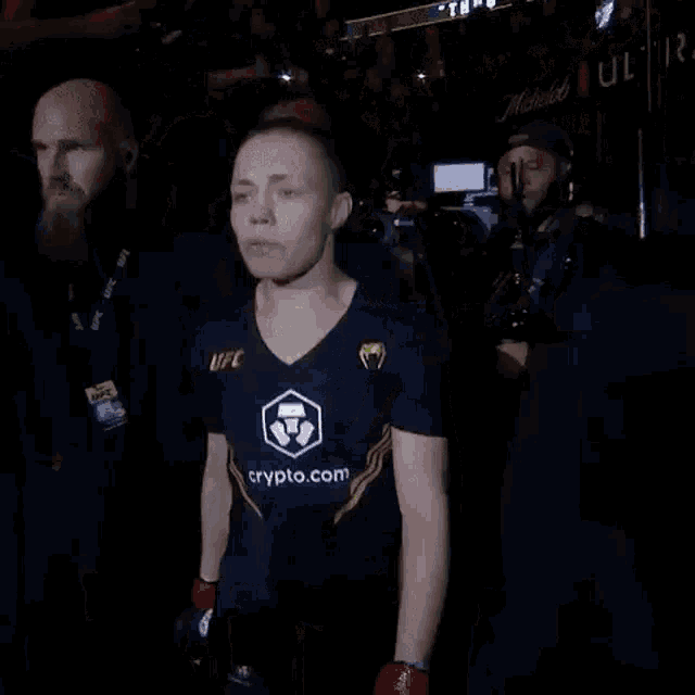 a woman in a blue shirt with the word crypto.com on it is walking out of a boxing ring .