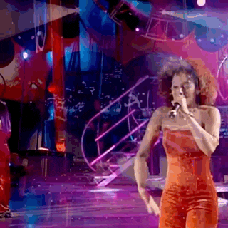 a woman in an orange jumpsuit is singing into a microphone on a stage .