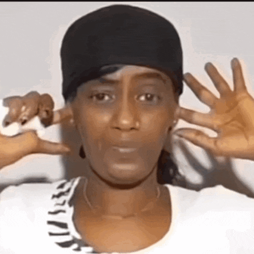 a woman is covering her ears with her hands while wearing a hat .