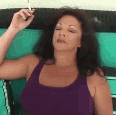 a woman wearing a purple tank top is smoking a cigarette