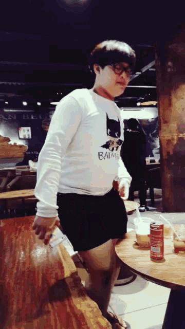 a person wearing a batman shirt stands in front of a wooden table