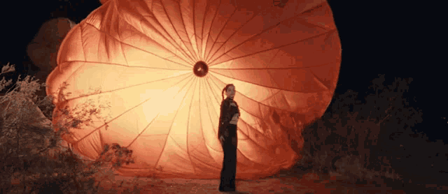 a woman in a black dress is standing in front of an orange parachute
