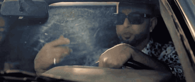 a man wearing sunglasses is smoking a cigarette in a car