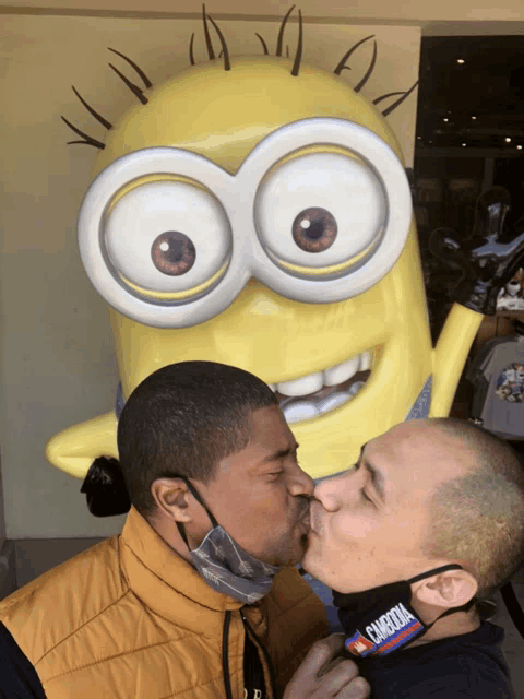 two men are kissing in front of a minion statue