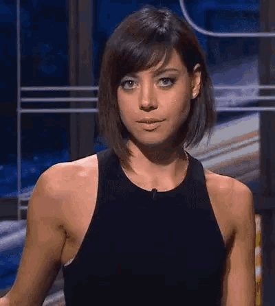 a woman with short hair is wearing a black tank top and standing in front of a window .