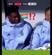 two soccer players are sitting in the dugout with a rainbow flag in the background and a question mark in red
