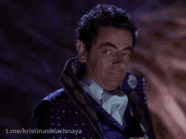 a man in a blue suit is standing in front of a dark background with kristinaoblachnaya written below him
