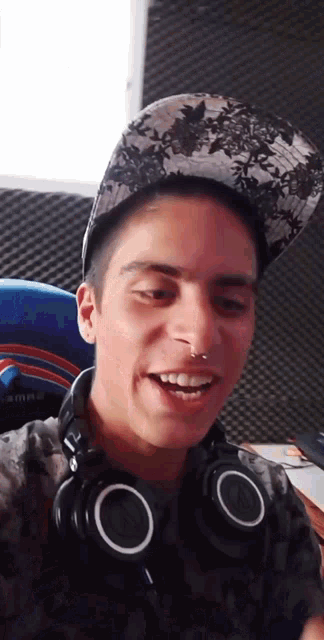 a young man wearing headphones and a hat smiles