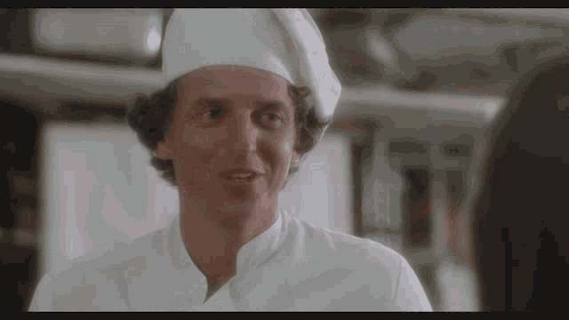 a man wearing a chef 's hat is smiling at someone