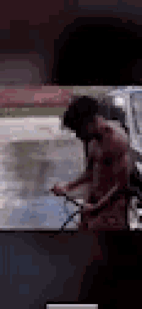a man without a shirt is washing a car with a hose .
