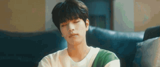 a young man is sitting on a couch with his eyes closed and a striped shirt on .