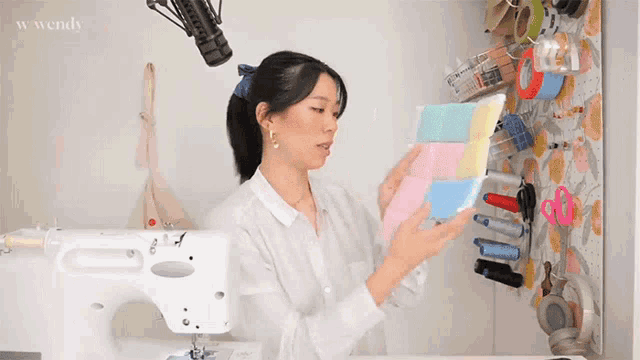 a woman is standing in front of a sewing machine and holding a piece of fabric
