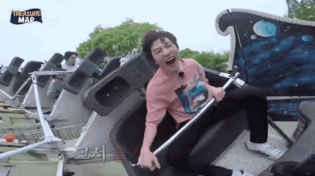 a man in a pink shirt is riding a roller coaster with a sign that says " treasure map "