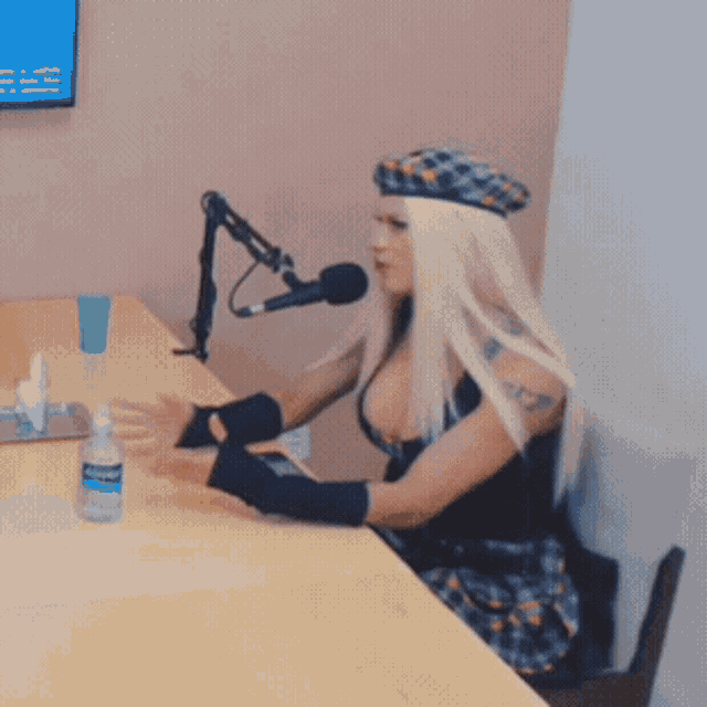 a woman sits at a table with a microphone and a bottle of hand sanitizer