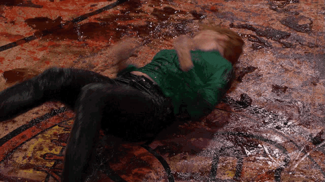 a man in a green shirt is laying on a dirty floor