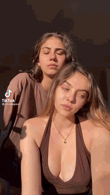 two women are posing for a picture with their eyes closed . one of the women is wearing a very low cut tank top .