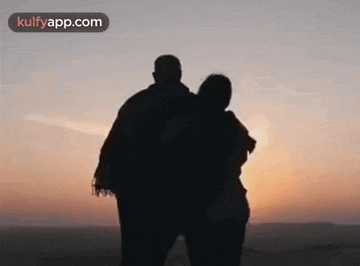 a man and a woman are standing next to each other looking at the sunset .