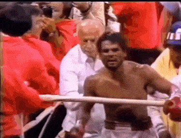 a man without a shirt is standing in a boxing ring surrounded by people