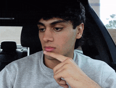 a man in a grey shirt is sitting in a car with his finger on his chin