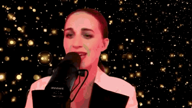 a woman singing into a shure microphone in front of a starry background