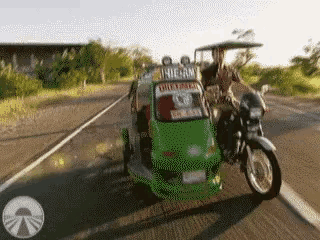 a motorcycle is driving down a road next to a green vehicle that says ' rickshaw ' on it