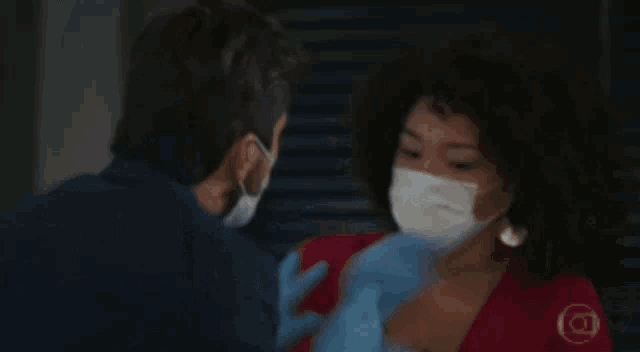 a man wearing a mask and a woman wearing gloves are standing next to each other .