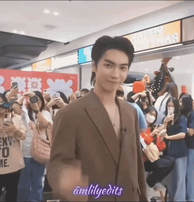 a man in a brown jacket is standing in front of a crowd of people taking pictures of him