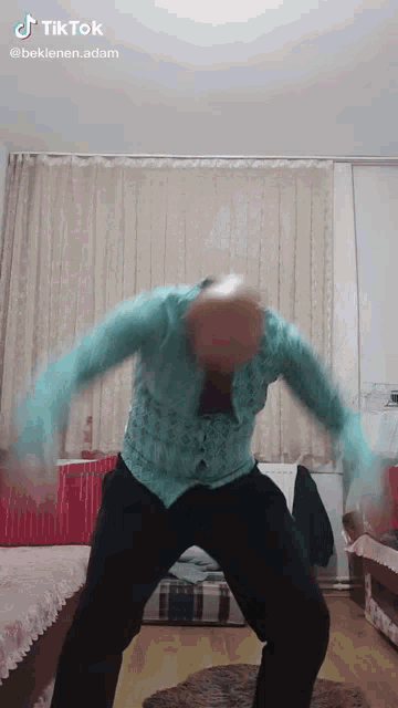 a man in a blue shirt and black pants is dancing in a room with a tiktok watermark above him