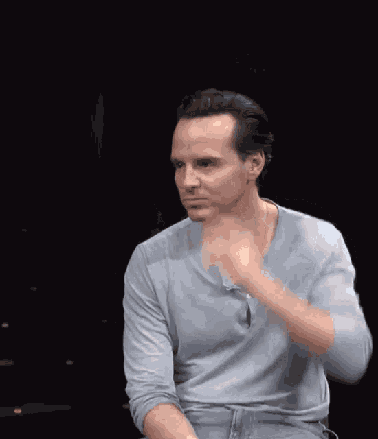 a man in a grey shirt is adjusting his hair in a dark room