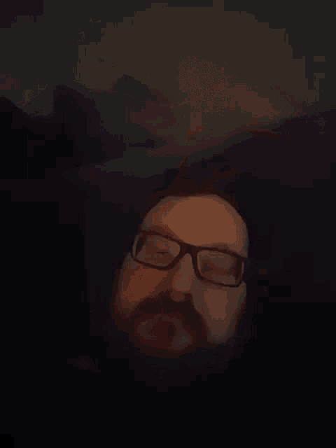 a man with glasses and a beard is laying on a couch .
