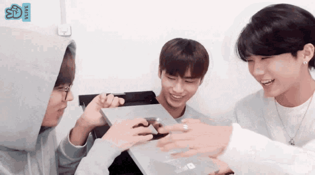 a group of young men are gathered around a laptop with vlive written on the bottom right