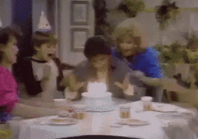 a group of people sitting around a table with a birthday cake on it