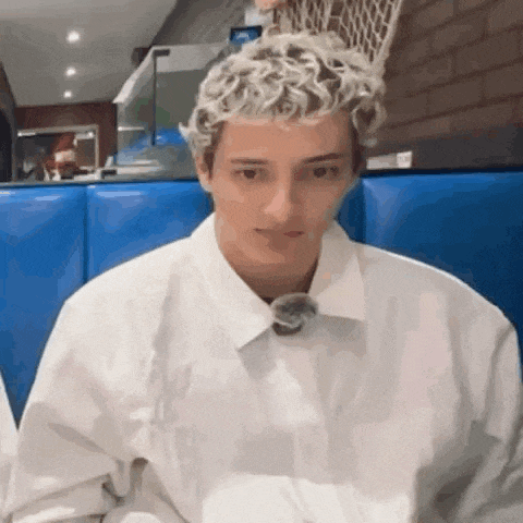 a young man with curly blonde hair is sitting in a blue booth .