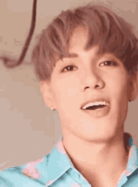 a close up of a young man with pink hair and a blue shirt .