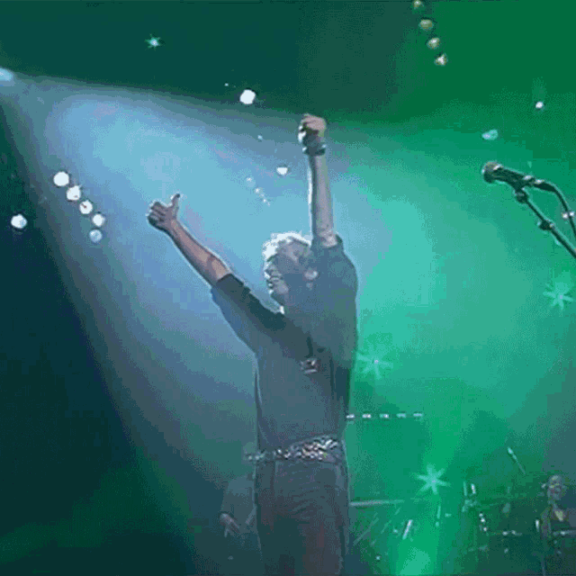 a man singing into a microphone on a stage with his arms in the air